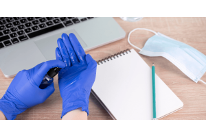  A person wearing blue gloves is typing on a laptop, focused on their work.