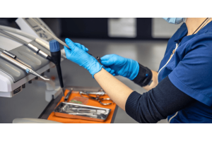 A woman wearing blue gloves is using a dental tool, focused on a dental procedure.