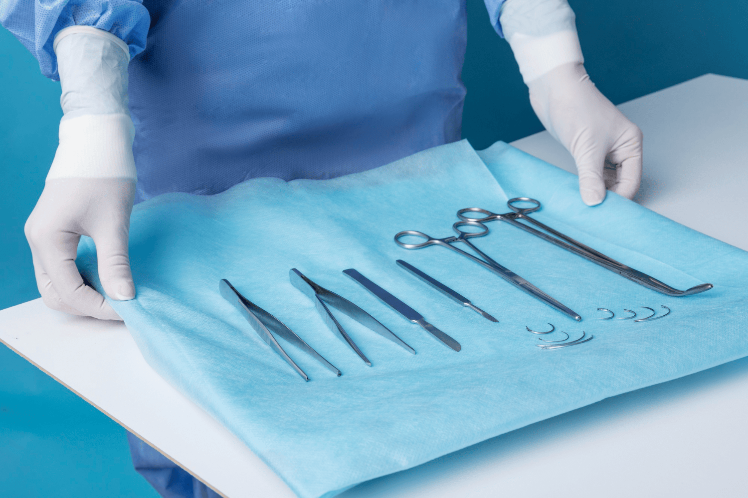 Surgical instruments, including forceps, scalpels, scissors, and curved needles, laid out on a sterile blue surgical drape.